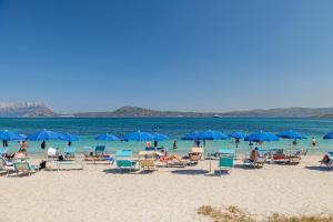 a group of people sitting on a beach with blue umbrellas at Hotel Mare Blue in Olbia