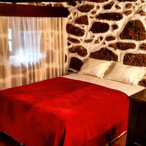 a bedroom with a red bed with a stone wall at Dona Gracia Belmonte in Belmonte