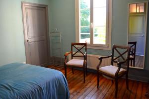 a bedroom with two chairs and a bed and two windows at Le Gîte des Sureaux in Rarécourt