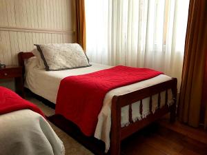 - une chambre avec un lit doté d'une couverture rouge et d'une fenêtre dans l'établissement Hospedaje Mery, à Cañete
