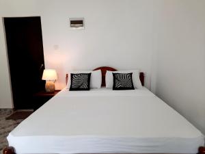 - une chambre avec un lit blanc et des oreillers noirs et blancs dans l'établissement Dream Villa Sigiriya, à Sigirîya
