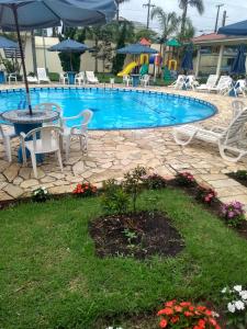 a pool with chairs and a table and an umbrella at Rota do Sol Praia Hotel in Guaratuba