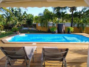 a swimming pool in a backyard with two chairs and a table at Villa & Bungalow Fleur de Coco in Sainte-Anne