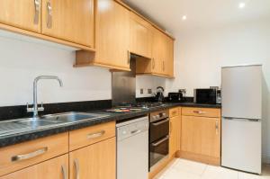 cocina con armarios de madera y nevera blanca en Atlas House - Ideal for Contractors or Derby County Fans en Derby