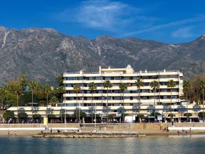 a hotel on the beach with mountains in the background at Beach Front Apartment-1st Line in Marbella