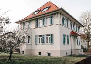 a white house with a red roof and green shutters at Ferienwohnung am Federsee in Bad Buchau
