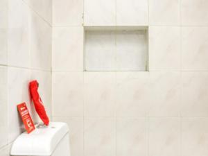 a white tiled bathroom with a red phone on a toilet at RedDoorz Syariah @ Lempuyangan in Yogyakarta +16 photos
