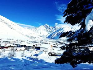 een dorp bedekt met sneeuw met bergen op de achtergrond bij Chalet Pkhelshe in Kazbegi