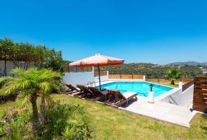 a villa with a swimming pool with chairs and an umbrella at Kolymbia Village in Kolymbia