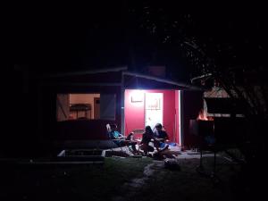 tres personas sentadas frente a una casa por la noche en La Casita de Monte en Monte Hermoso