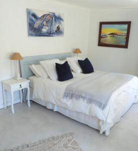 a white bedroom with a large white bed and a table at Weavers' Cottage in Gordonʼs Bay