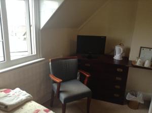 a bedroom with a chair and a dresser with a television at Park House Guest House in Warwick