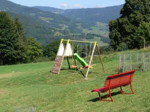 un banco rojo sentado en un campo con un parque infantil en Gîte la Sapinière, en Labaroche