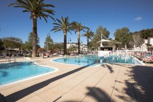 a pool at a resort with palm trees at Minura Cala Galdana & Apartamentos d'Aljandar in Cala Galdana