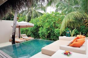 a patio area with a pool, chairs, and an umbrella at Ayada Maldives in Gaafu Dhaalu Atoll