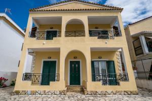 a yellow house with green doors and a balcony at Barax Apartments in Agios Georgios