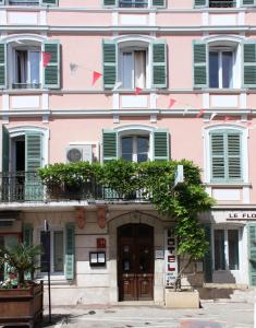 un edificio rosa con ventanas con persianas verdes y una puerta en Hotel Le Flore en Fréjus