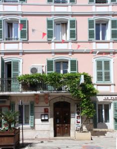 un bâtiment rose avec des fenêtres vertes à volets et une porte dans l'établissement Hotel Le Flore, à Fréjus