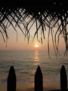 a sunset over the ocean from a beach with a straw roof at The Madampa Sea Side Lodge in Ambalangoda