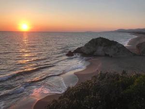 a sunset over a beach with a rock in the ocean at Sabbie d'oro in Gela