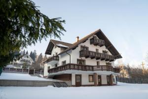 Una gran casa blanca con balcones de madera en la nieve. en Vila Molidul Zarnesti, en Zărneşti