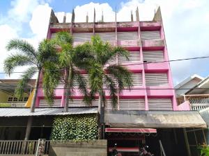 różowy budynek z palmami przed nim w obiekcie OYO 3116 Batu Putih Homestay w mieście Makasar