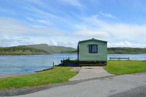 un petit bâtiment vert à côté d'une masse d'eau dans l'établissement Sunnybrae, Isle of Luing, à Cullipool