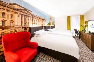 Cette chambre d'hôtel comprend 3 lits et un fauteuil rouge. dans l'établissement Millennium Gloucester Hotel London, à Londres