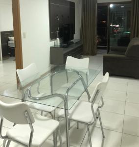 una mesa de cristal y sillas blancas en la sala de estar. en Flat em Cabo Branco, en João Pessoa