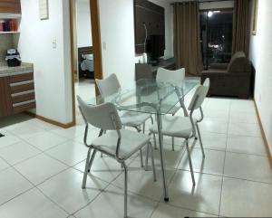 uma mesa de vidro e cadeiras brancas numa sala de estar em Flat em Cabo Branco em João Pessoa
