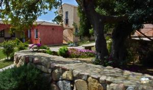 a stone wall in front of a house with a tree at Hotel La Corte Rosada in Villasimius