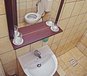 a bathroom with a sink and a toilet with glasses on a shelf at Cazare Karmina in Baia Mare