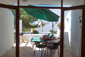 un patio con mesa, sillas y una sombrilla verde en B13-Dúplex luminoso+ piscina a 150 m del mar, en Charco del Palo