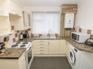 a kitchen with white cabinets and a sink and a microwave at Cwtch Ar Y Mor in Burry Port