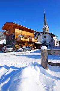 un edificio ricoperto di neve con una chiesa sullo sfondo di Gasthof Zacherlbräu a Bruck an der Grossglocknerstrasse