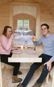un hombre y una mujer sentados en una mesa en una cabaña en Helshovens wijnvat, en Borgloon