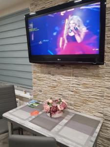 a tv on a stone wall with a table with flowers at Crystal Apartment in Gulbene