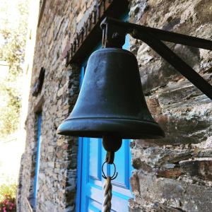 eine Glocke hängt von einem Gebäude mit einem blauen Fenster in der Unterkunft Casa da Padaria in Piódão