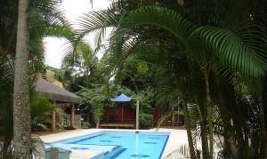 a swimming pool with palm trees in front of a house at JuquehyRoots AC vent em 4suítes 2 gelad salas banho térreos churrasq wifi jard filtro água estac terraço panorâm privativos piscina coletiva condo fech boa localizaçã SEM roupa cama mesa banho in Juquei