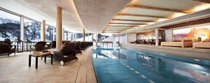 een zwembad met stoelen en een persoon op een stoel ernaast bij Hotel Berghof Crystal Spa & Sports in Tux