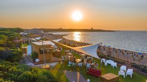 un grupo de personas sentadas en mesas en una playa al atardecer en Camping Village Baia Blu La Tortuga en Aglientu