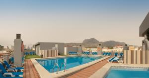 a pool on the roof of a hotel with blue chairs at Hotel Olympus in Benidorm