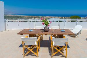 una mesa de madera con sillas blancas y un jarrón con flores en Litsa Holiday Home, en Kalathos