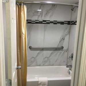 baño con bañera blanca y cortina de ducha de mármol en Travel Inn & Suites, en Humble