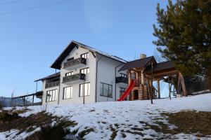 a white house with a red slide in the snow at PENSIUNEA ARINAS in Vatra Dornei
