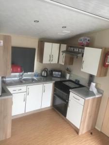 a small kitchen with white cabinets and black appliances at Take me to the beach at J&S caravan holidays Newquay Bay resort in Saint Columb Minor