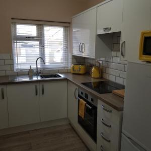 uma cozinha com armários brancos, um lavatório e um fogão em Chynoweth Court em Newquay