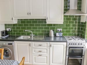 uma cozinha com armários brancos e azulejos verdes em Glor Cottage em Ballyhaunis