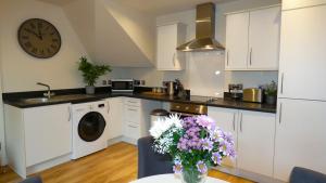 a kitchen with white cabinets and a clock on the wall at Three Storey Townhouse with Parking in Telford