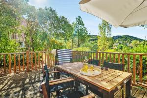 eine Holzterrasse mit einem Holztisch, Stühlen und einem Sonnenschirm in der Unterkunft Village Pierre & Vacances Le Rouret in Grospierres